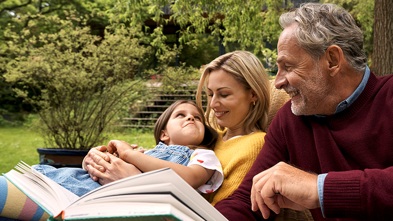 Opa, Mutter und Tochter lesen ein Buch im Garten