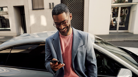 Mann mit Smartphone vor seinem BMW